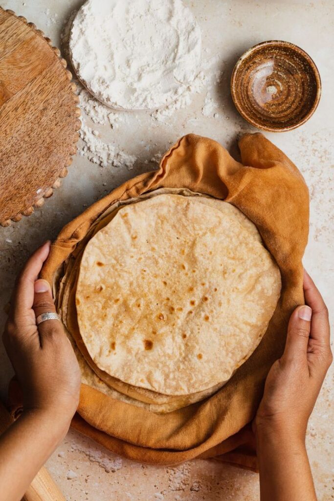 hands holding homemade chapatis in a kitchen…